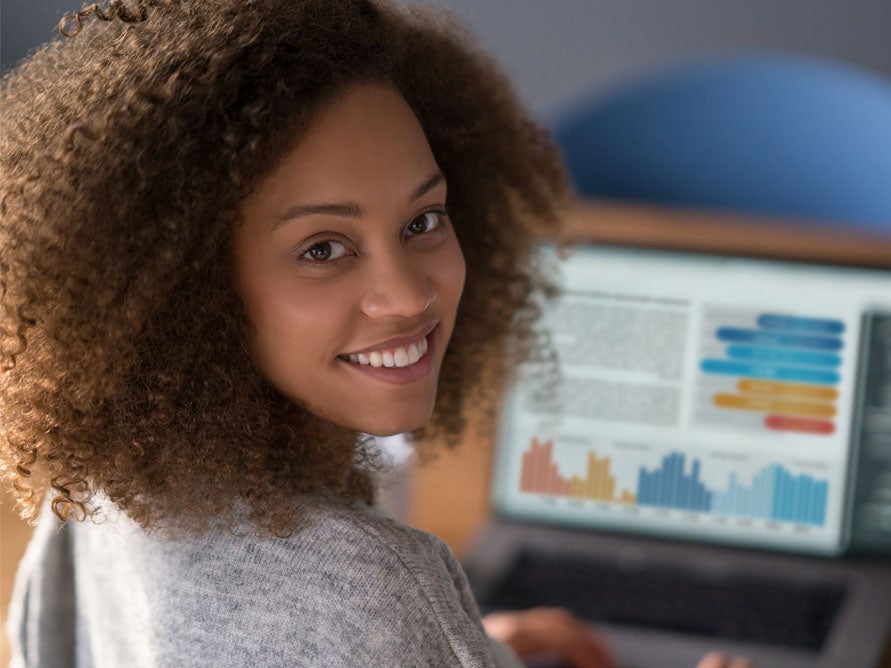 Student sitting at laptop with charts looking back at camera