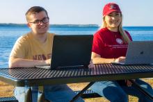 M/F students with computers at picnic bench with North Bay behind them