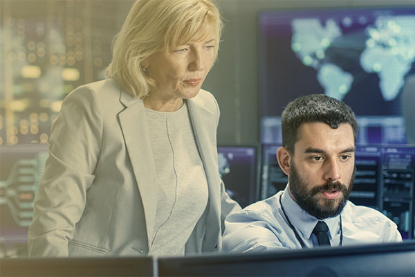 manager looking over the shoulder of colleague in situation room